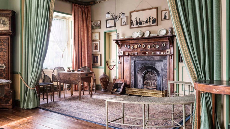 Inside of the drawing room at A la Ronde with a large fireplace and green curtains